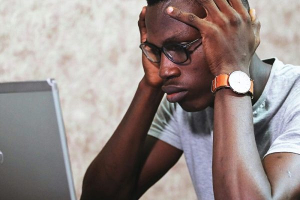 A man appears frustrated while working on a laptop in an office setting, showcasing remote work challenges.